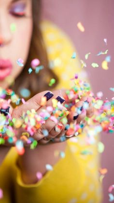 a woman blowing out sprinkles on her fingers and looking at the camera