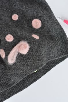 a knitted hat with pink polka dots on it and a needle next to it