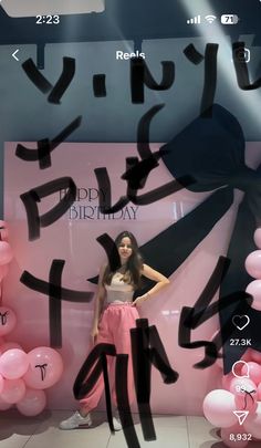 a woman standing in front of a display with pink balloons and black writing on it