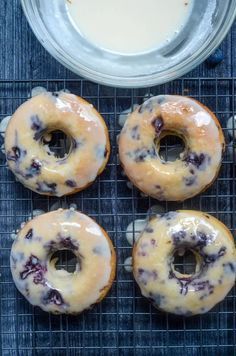 four blueberry donuts on a cooling rack next to a bowl of yogurt