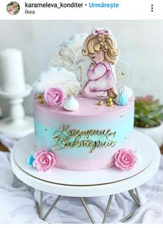 a pink and blue cake with an angel on top is sitting on a white table