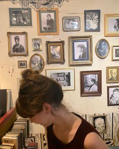 a woman sitting at a table in front of a wall with many framed pictures on it