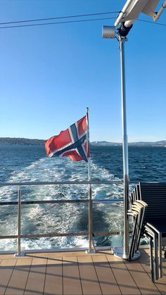 a flag flying on the side of a boat in the ocean next to a bench