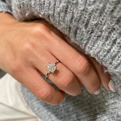 a woman's hand with a diamond ring on her left hand and a gray sweater