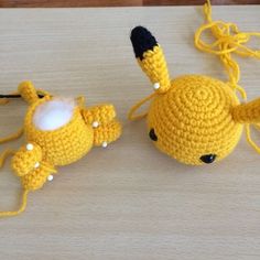 two small crocheted toys are sitting on a wooden surface, one is yellow and the other is white