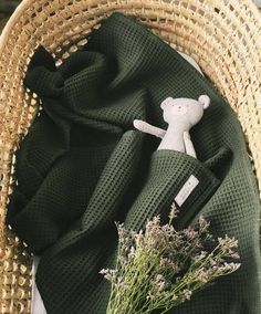 a teddy bear sitting on top of a green blanket next to a basket filled with flowers