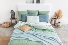 a bed with green and blue linens in a white room next to a painting on the wall