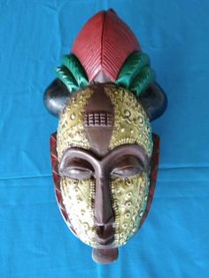 a wooden mask with green, red and gold decorations on it's face sitting on a blue background