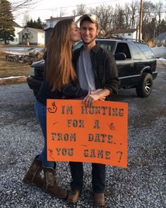 a man and woman standing next to each other holding an orange sign that says i'm hunting for a date you came?