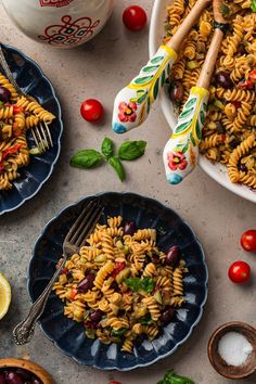 pasta salad with cherry tomatoes, olives and spinach on two plates next to a cup of coffee