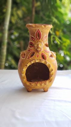 a decorative vase sitting on top of a white tablecloth covered table with trees in the background