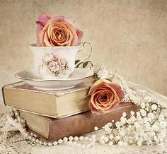 two books stacked on top of each other with roses in the cup and saucer