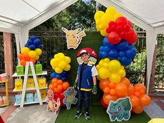 a young boy standing in front of a display of balloons and pokemon characters at a children's birthday party