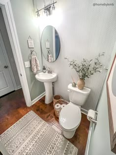 a white toilet sitting next to a sink in a bathroom on top of a hard wood floor