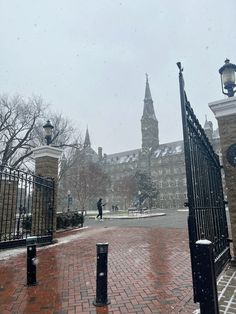 a person is standing in the snow near a gate and building with a clock on it