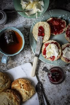 scones with jam and butter are on plates next to a cup of tea, spoon and knife