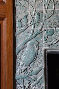 a decorative tile wall with an owl and tree design on it's side, in front of a wooden door