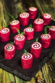 small red rolls are arranged on a black plate