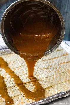 someone pouring caramel sauce over crackers on top of each other in a pan