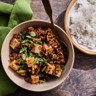 a bowl filled with rice and tofu next to another bowl full of rice on a wooden table