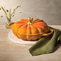 an orange pumpkin sitting on top of a white plate next to a green napkin and flowers