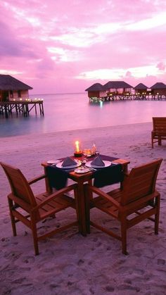 two wooden chairs sitting on top of a beach next to a table with plates and glasses