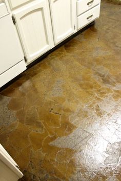 a kitchen with white cabinets and an old worn concrete floor that has been stained brown