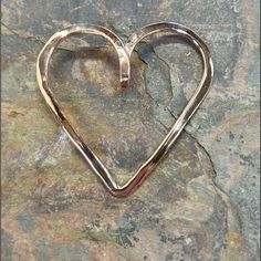 a heart shaped metal object sitting on top of a stone surface with the word love written in it