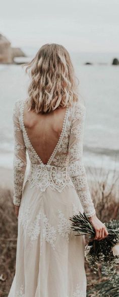 a woman in a white dress is standing near the ocean with her back to the camera