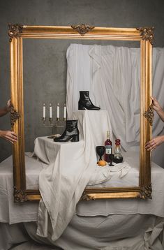 a person holding up a large mirror with shoes and candles on it in front of them