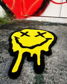 a smiley face rug on the ground in front of a wall with graffiti painted on it