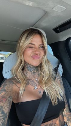 a woman with tattoos on her chest sitting in a car and looking at the camera