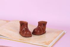 a pair of brown leather baby shoes sitting on top of a wooden table next to a book