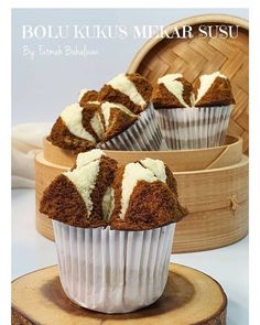 three cupcakes with white frosting sitting on top of a wooden stand next to a basket