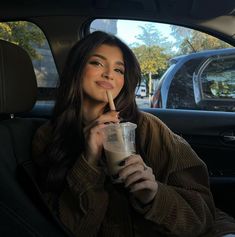 a woman sitting in the back seat of a car holding a drink and looking at the camera