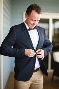 a man in a suit and bow tie is looking down at his jacket while standing outside