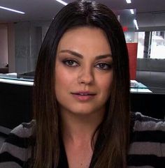 a woman with long brown hair is sitting in an office cubicle looking at the camera