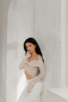 a woman leaning against a wall wearing a white dress