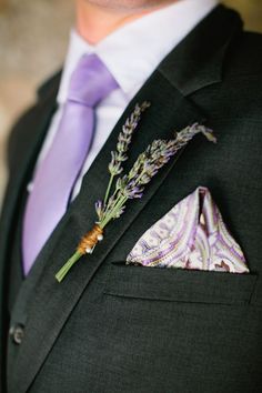 a man in a suit with a purple tie and lavender boutonniere on his lapel