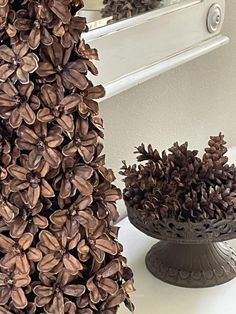 two vases filled with pine cones sitting on top of a white counter next to a mirror