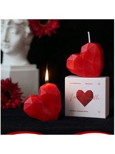 two red hearts sitting on top of a box next to a candle