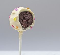 a chocolate cake ball on a stick with sprinkles and white frosting