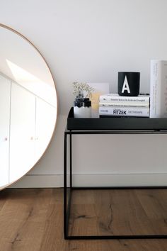 a black table topped with books next to a round mirror on top of a wooden floor