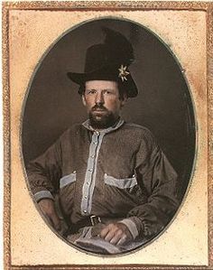 an old time photo of a man with a hat and beard wearing a long sleeved shirt