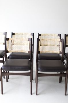 a set of four chairs with woven backrests and black leather seats, in front of a white wall