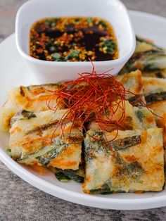 a white plate topped with food next to a bowl of dipping sauce