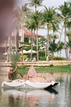 a bride and groom in a small boat on the water with palm trees behind them