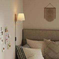 a bed room with a neatly made bed next to a wall mounted lamp and pictures on the wall