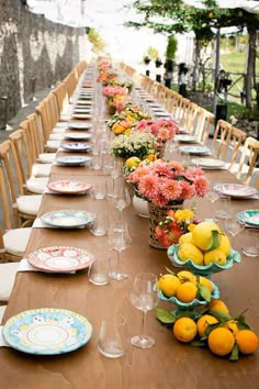 a long table with plates and vases filled with oranges, lemons and pink flowers