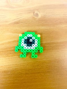 a green and white beaded object sitting on top of a wooden table next to a cell phone